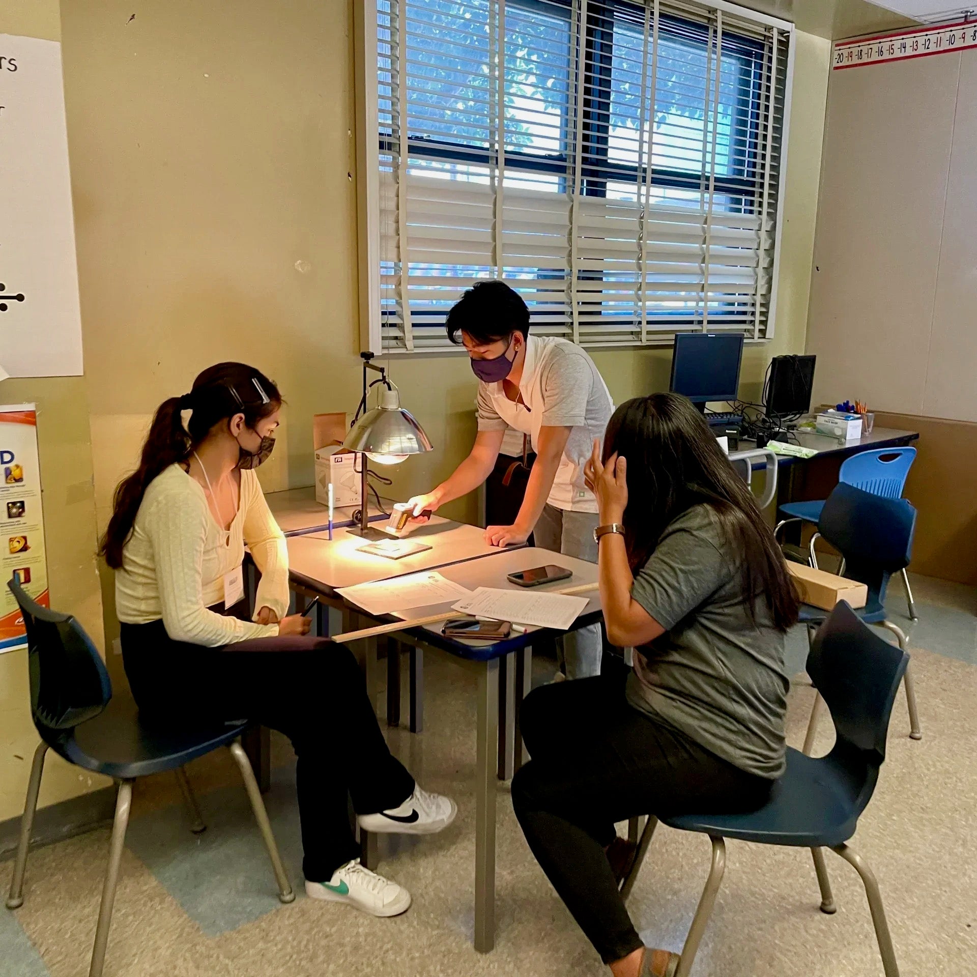 The image displays two undergraduate mentors and a teacher working together on the Grade 7 Heat Islands investigation.